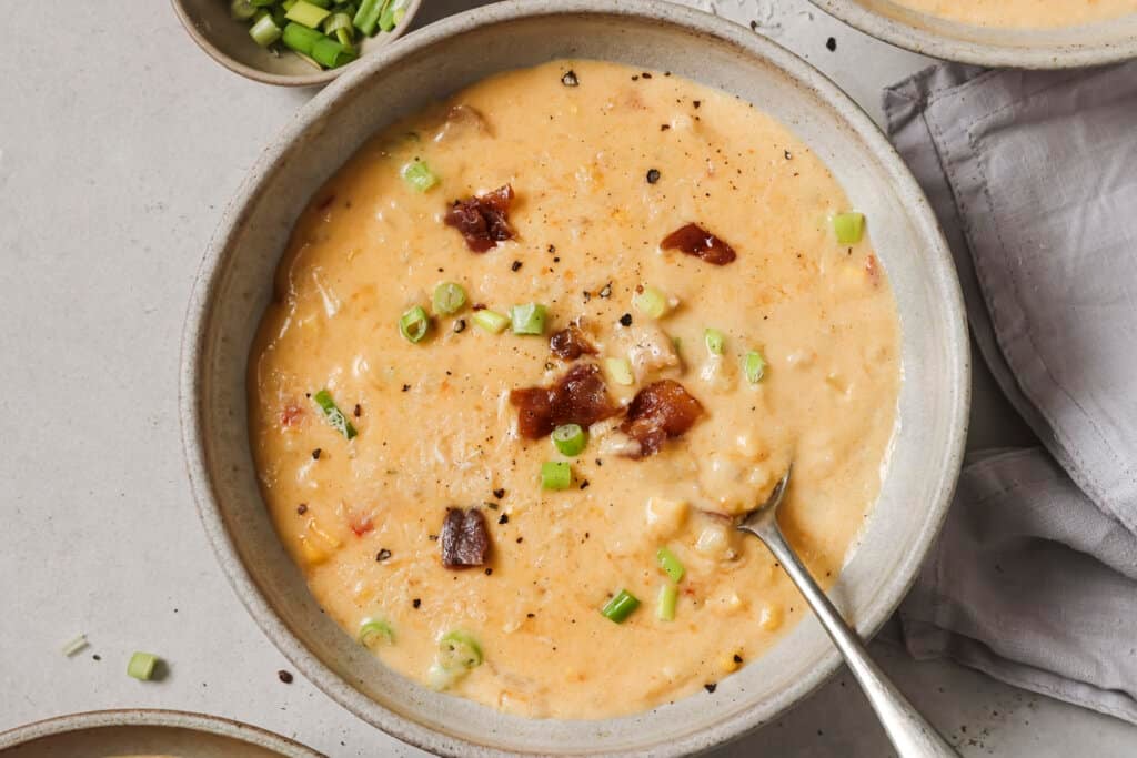 a bowl of roasted corn chowder with a spoon in it.