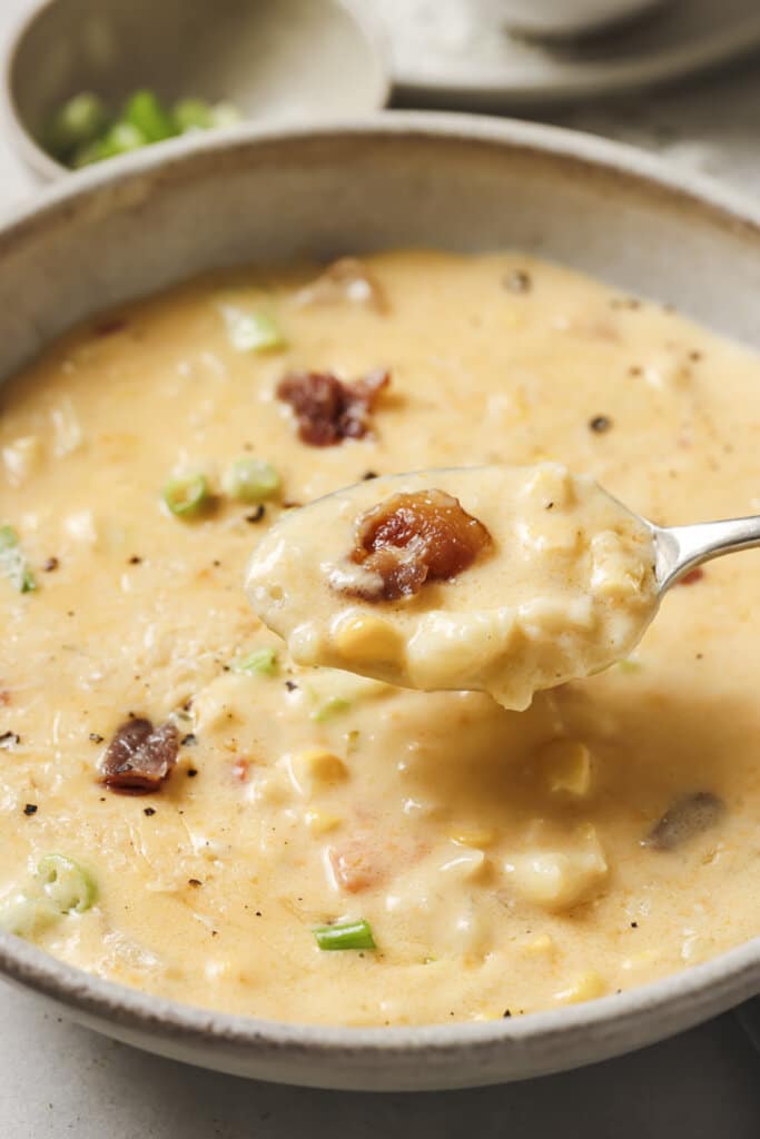 close up of roasted corn chowder on a spoon, held over a bowl of chowder