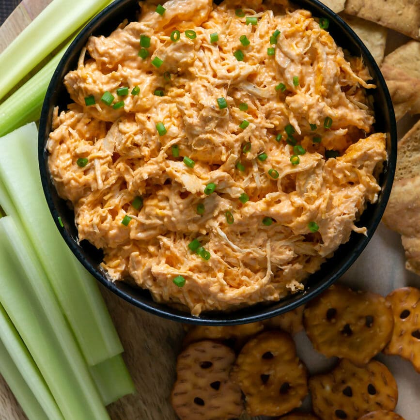 slow cooker buffalo chicken dip in a black bowl with celery and pretzels