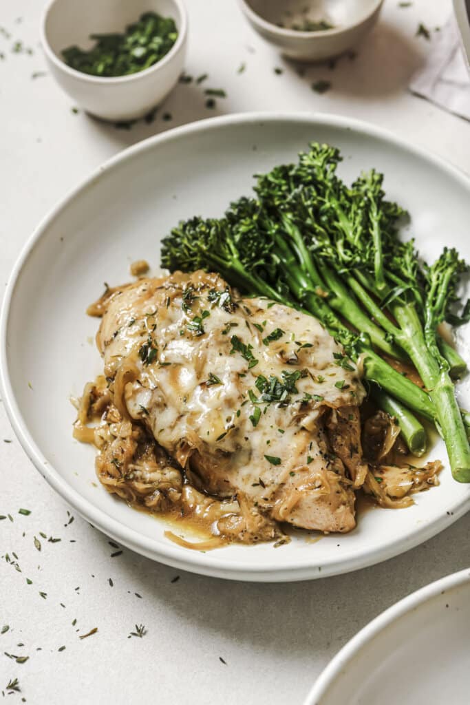 a piece of french onion chicken on a white plate with broccolini