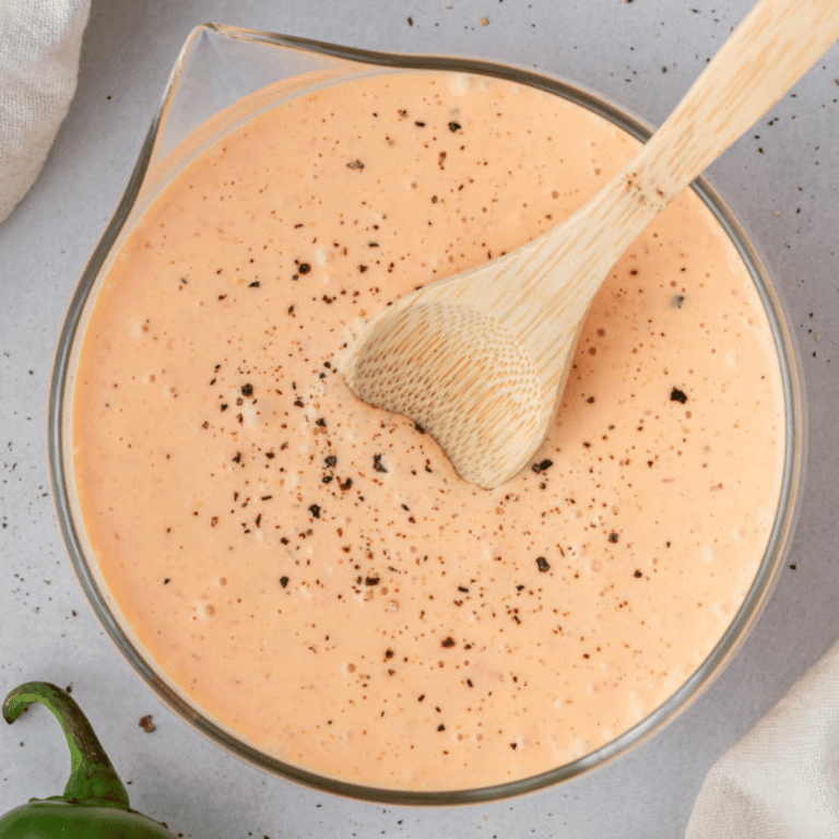 baja sauce in a glass container with a wooden spoon inside