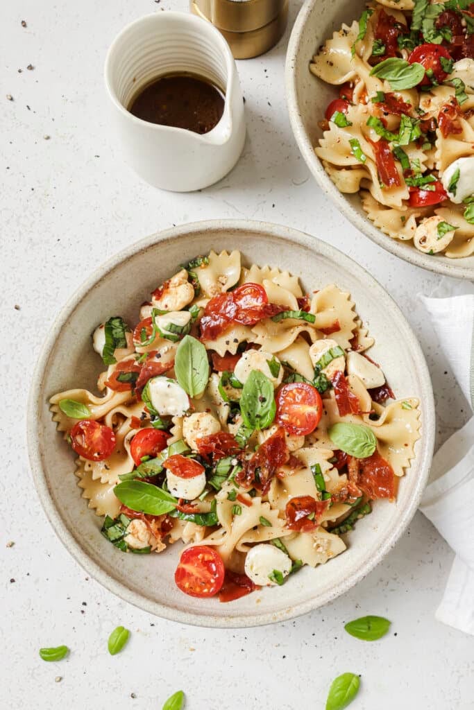 Caprese pasta salad in a white bowl with extra dressing on the side.