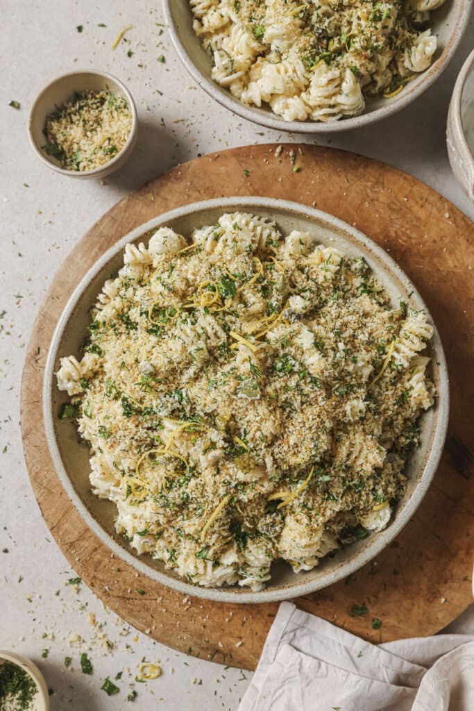 A bowl of dill pickle pasta salad on a wooden cutting board.