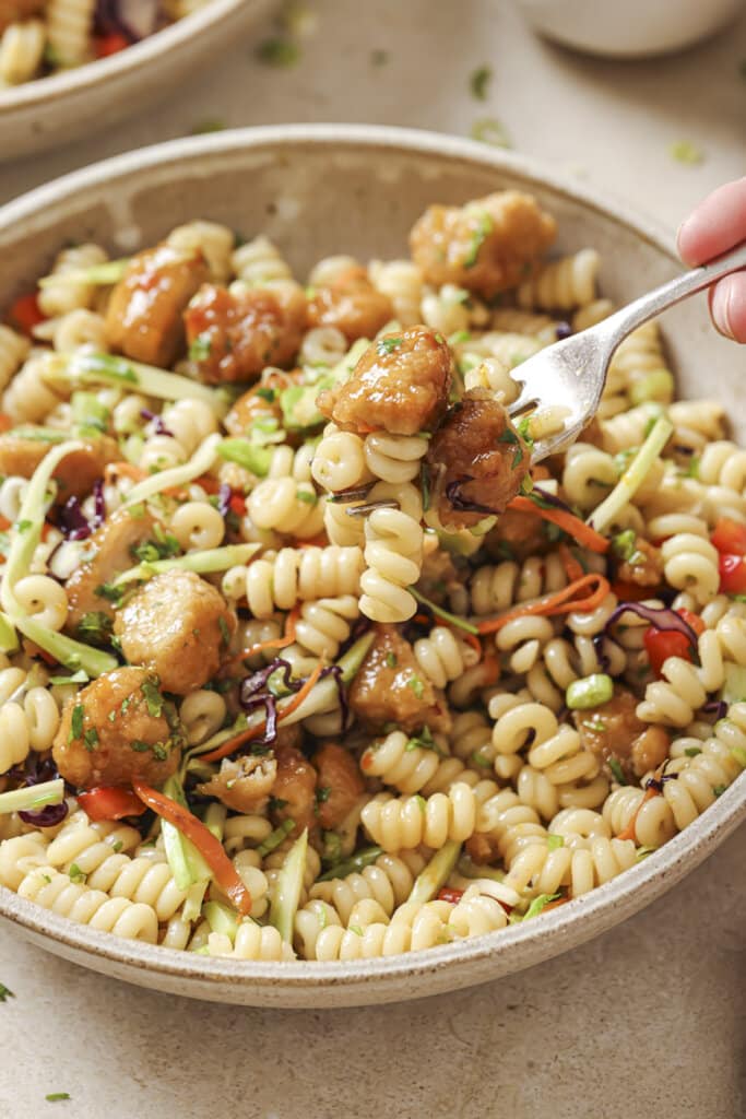 Scooping a forkful of orange chicken pasta salad from a bowl.