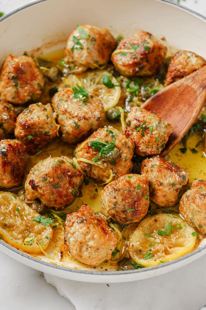 chicken piccata meatballs in a white pan with a wooden spoon