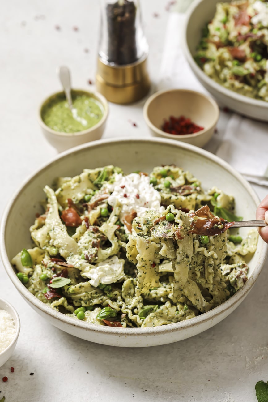 Taking a forkful of pesto prosciutto pasta from a bowl.