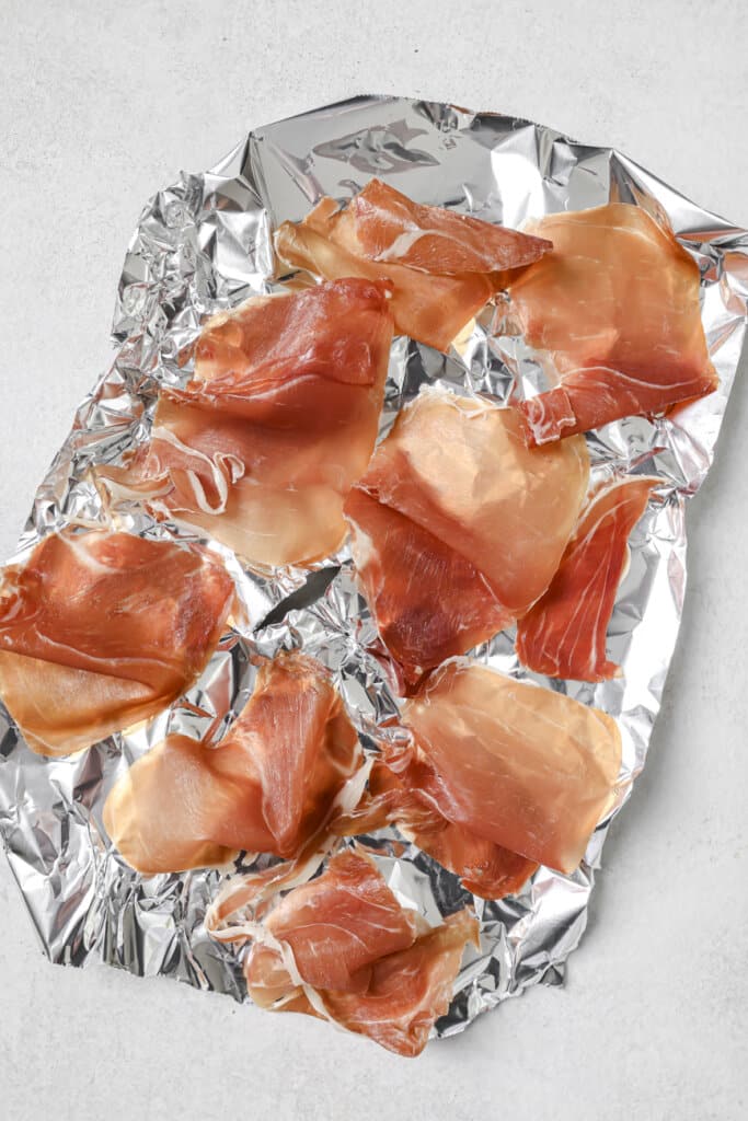 Placing pieces of prosciutto on a baking sheet covered with foil.