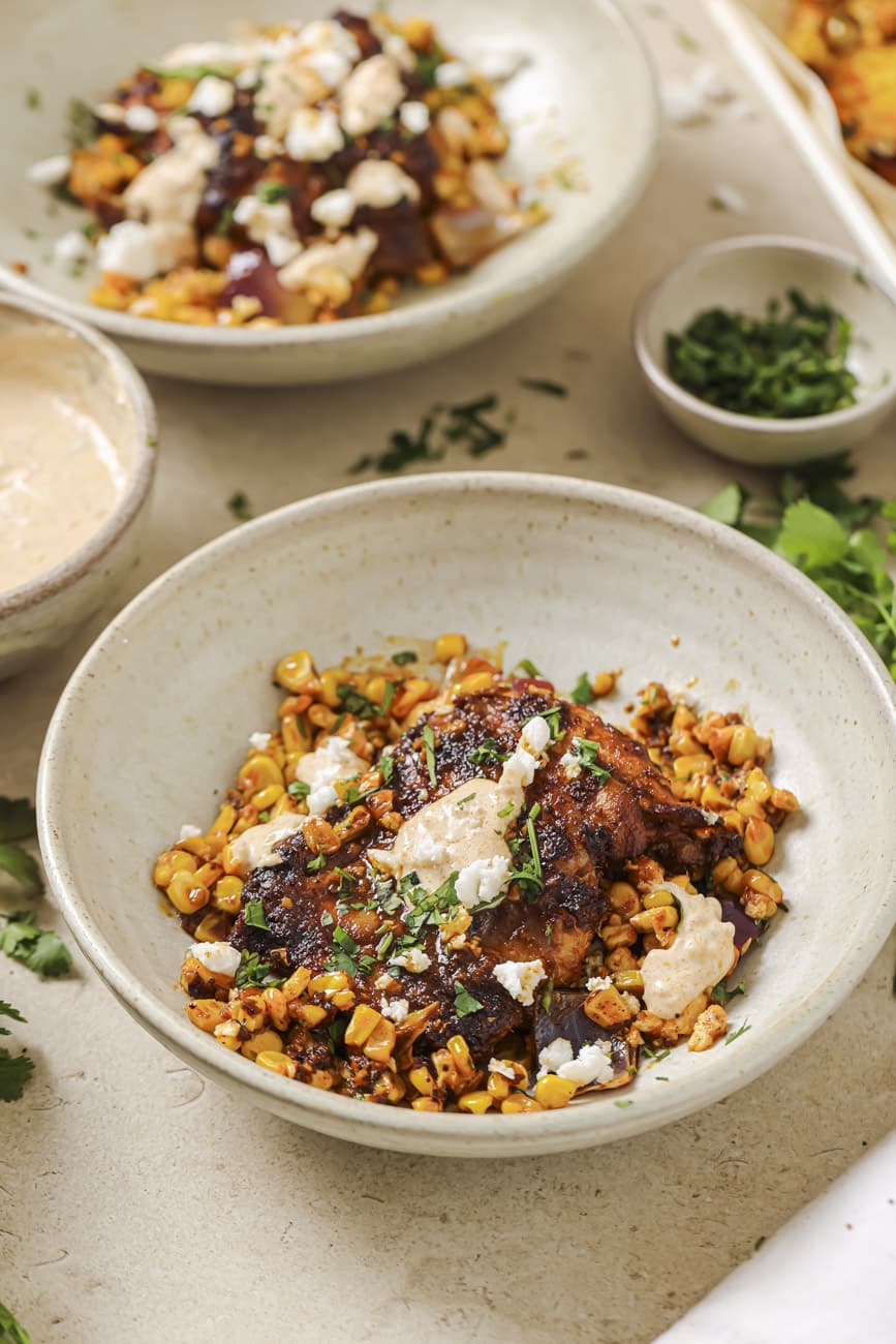 A bowl with sheet pan chicken thighs and corn.