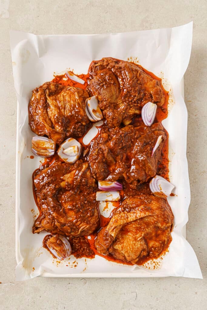 Chicken thighs and red onions on a baking sheet lined with parchment paper.