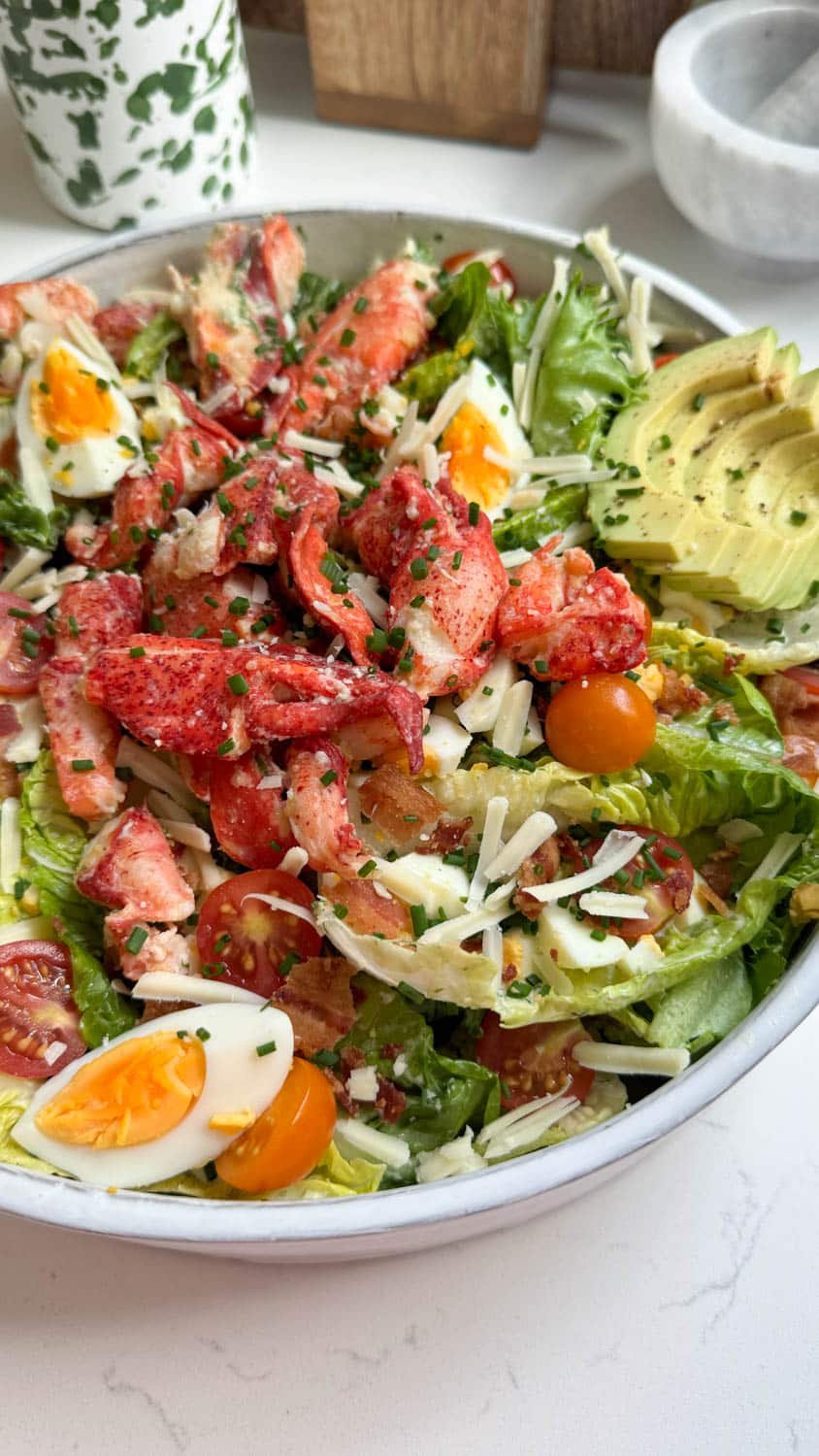 lobster salad in a large white bowl topped with sliced avocado and hard boiled eggs.