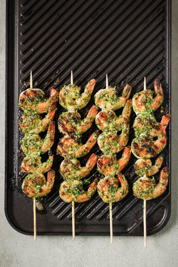 shrimp on wooden skewers cooking on a grill top.