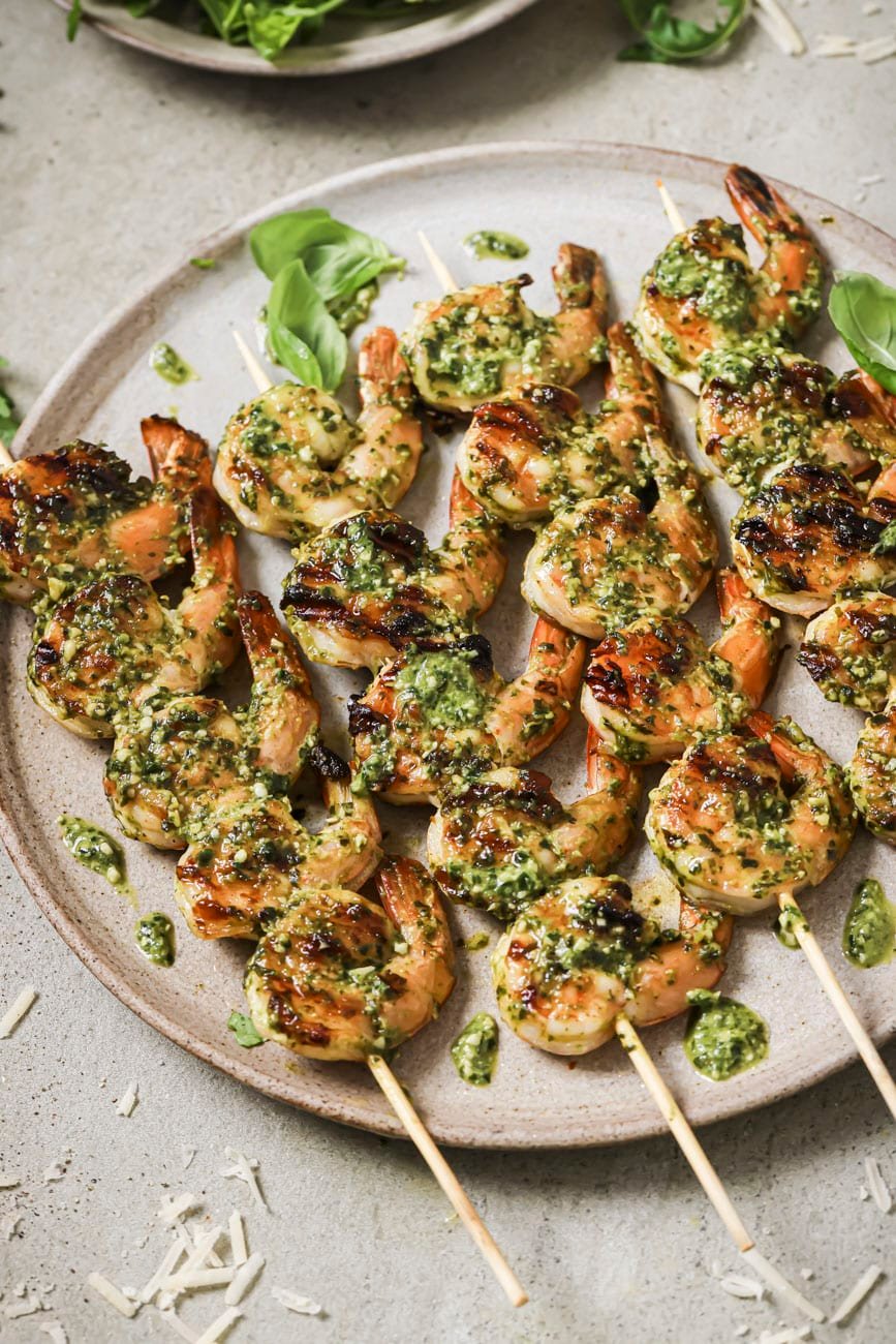 grilled pesto shrimp on a white plate with arugula leaves.