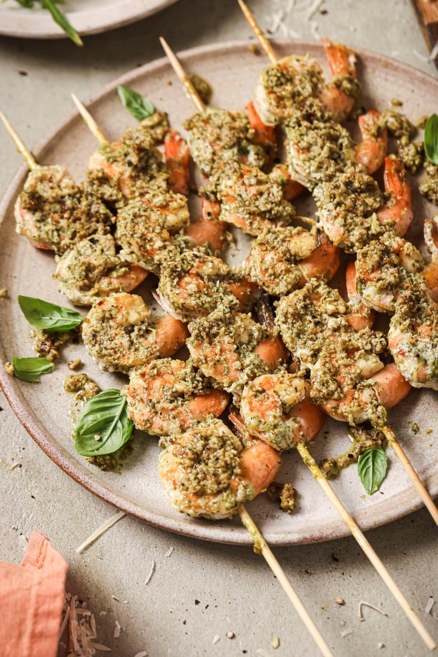 A plate of perfectly grilled pesto shrimp on wooden skewers.