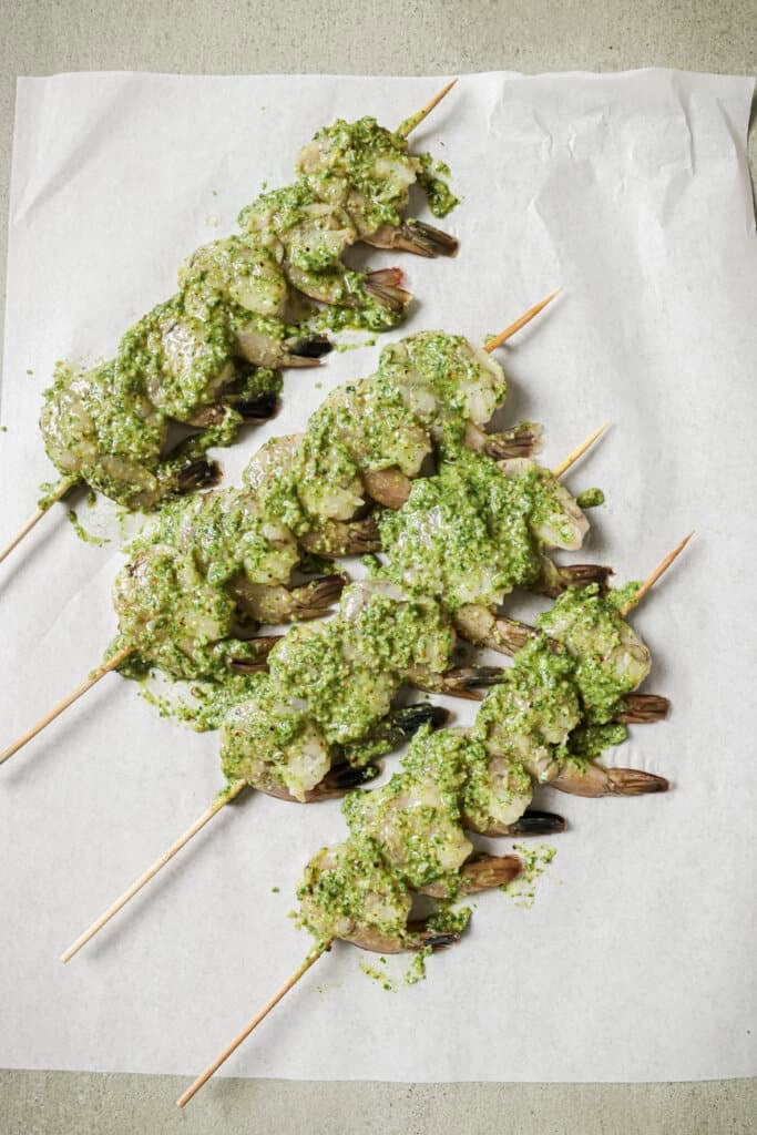 Raw shrimp on skewers covered in pesto.