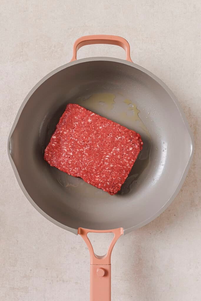 Cooking ground beef in a skillet with oil.