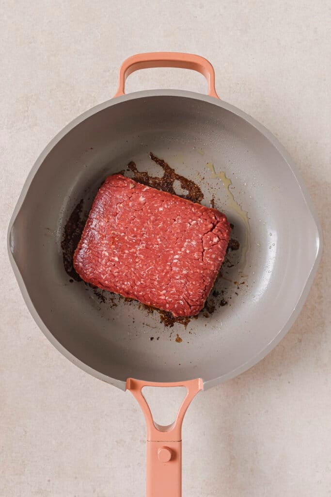 Cooking ground beef in a skillet with oil.