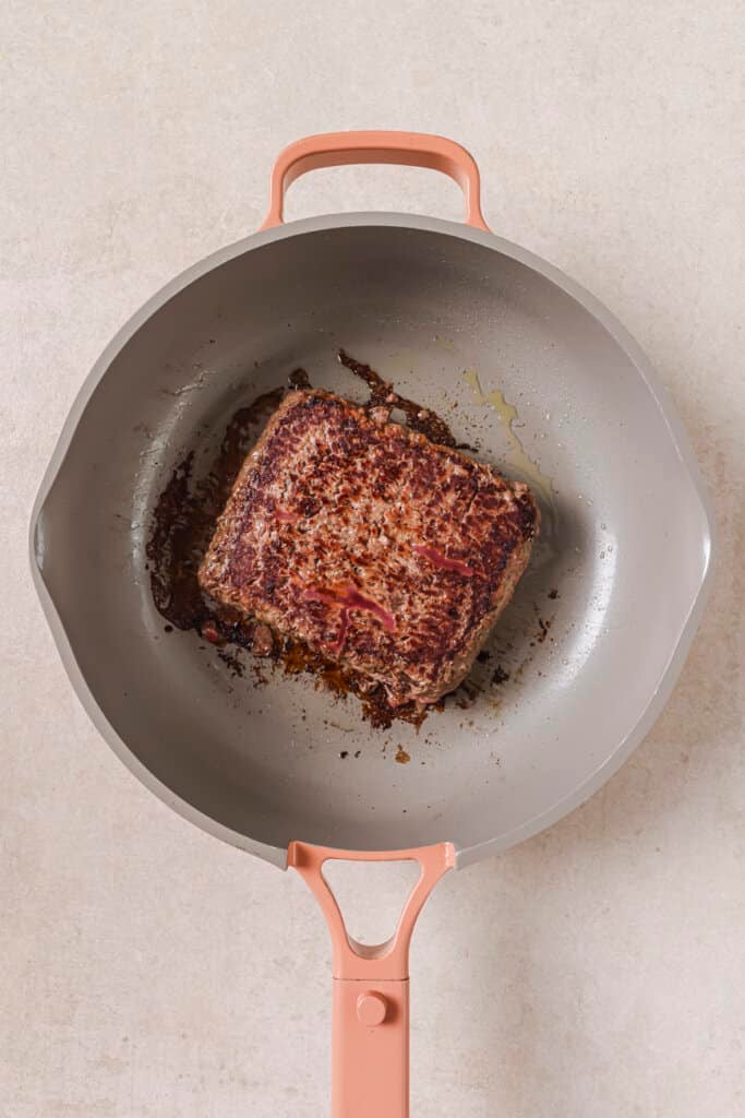 Partially browned ground beef in a skillet with oil.