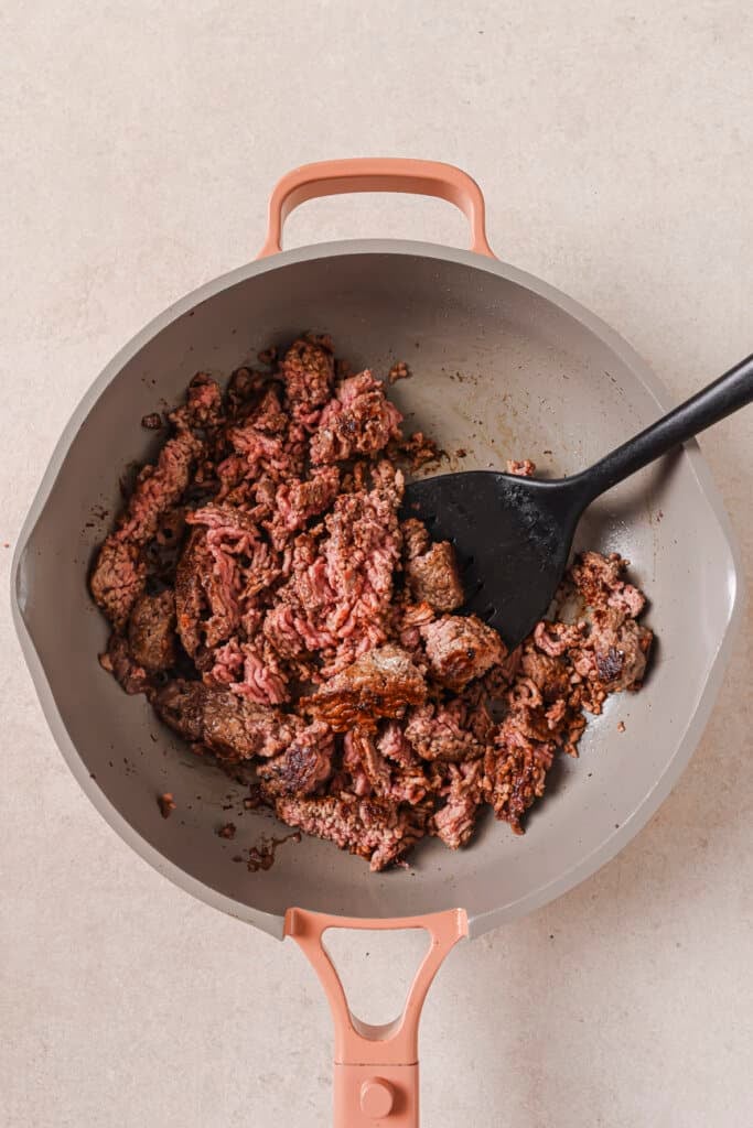 Using a spatula to break up ground beef in a skillet.