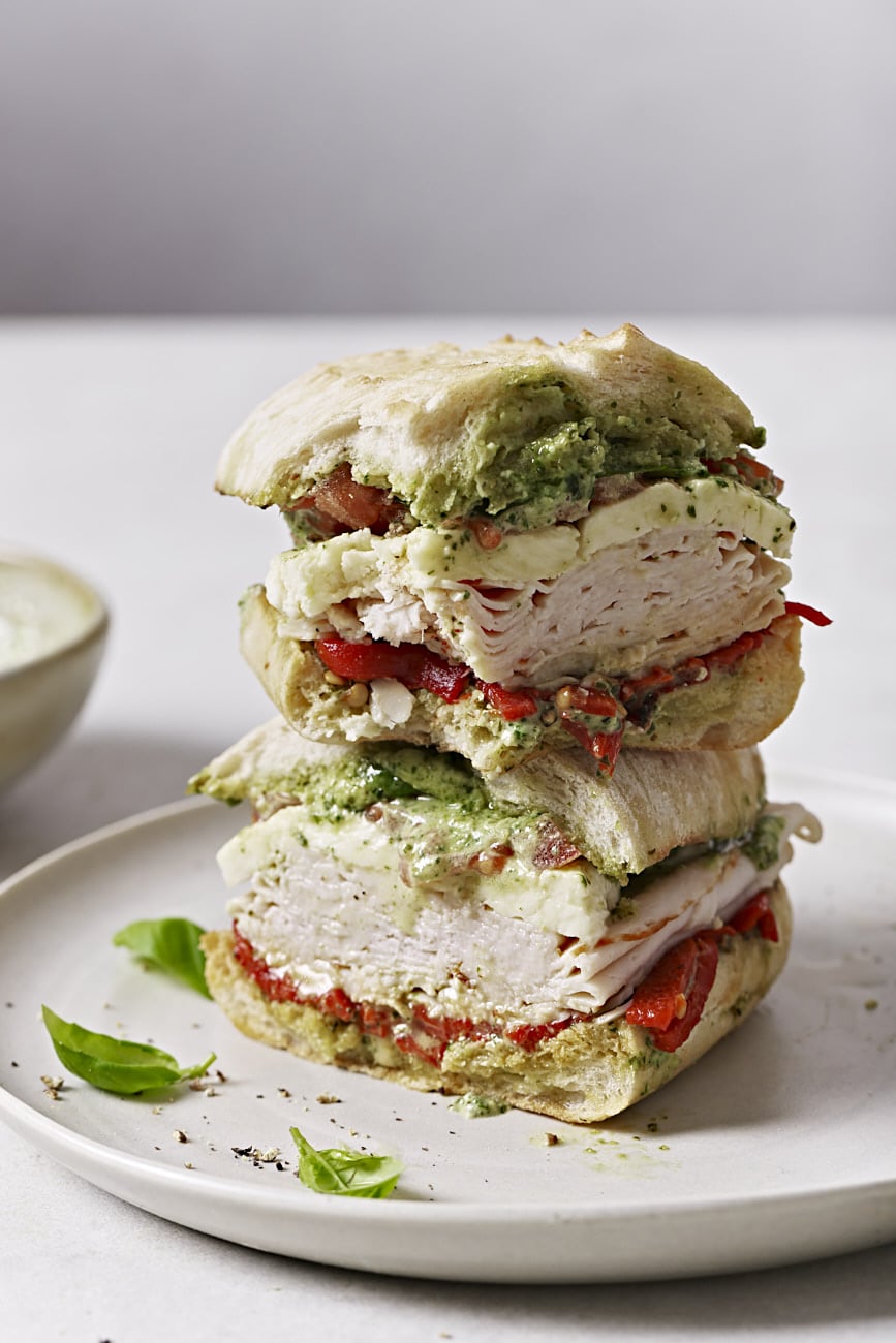 Two halves of turkey sandwich stacked on top of each other on a plate.