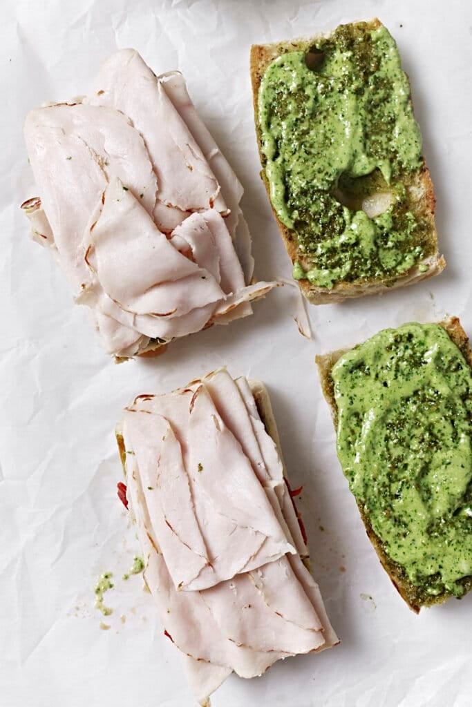 Adding turkey and more spread to pesto covered bread.