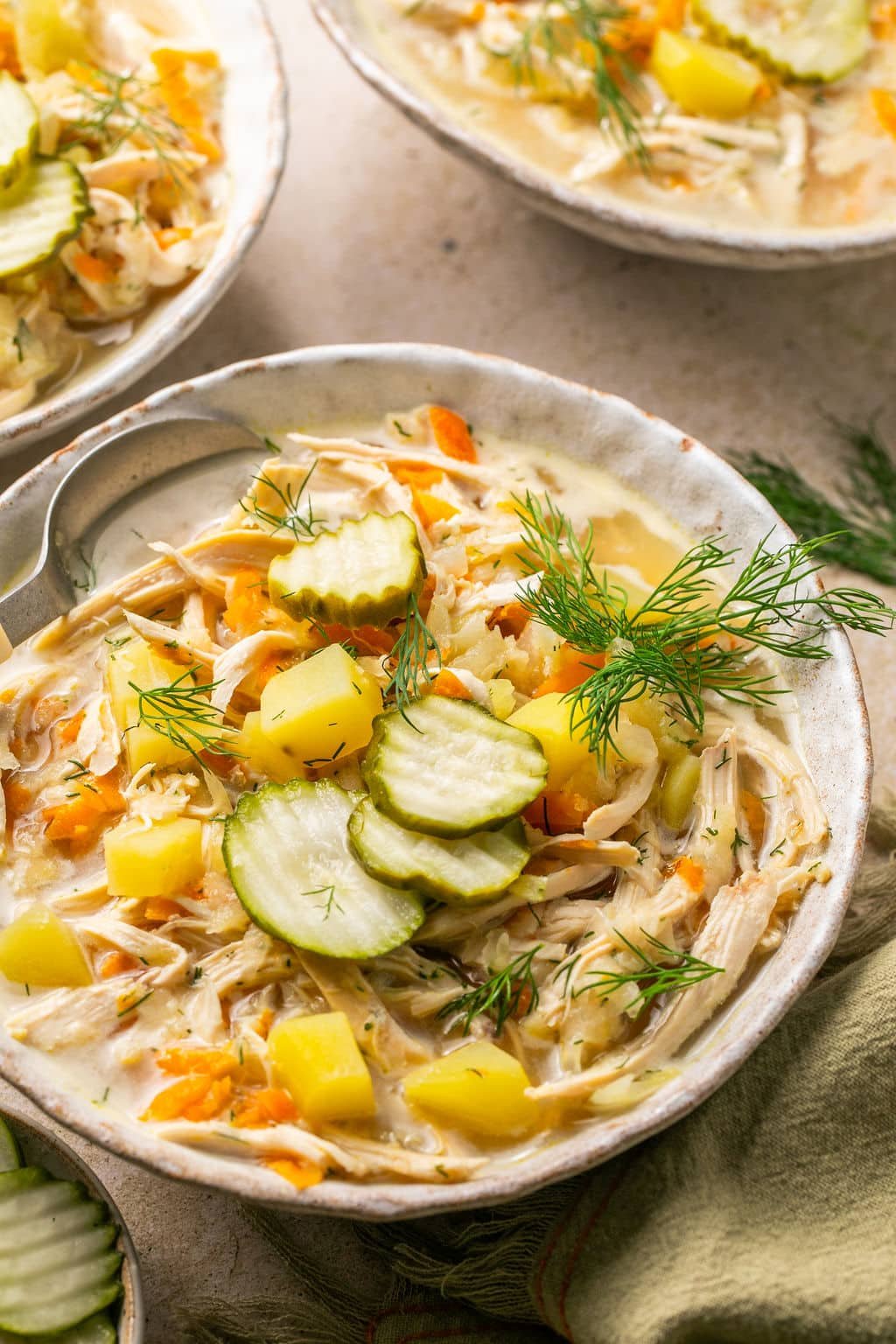 Top down view of a bowl of dill pickle soup surrounded by other bowls of soup.