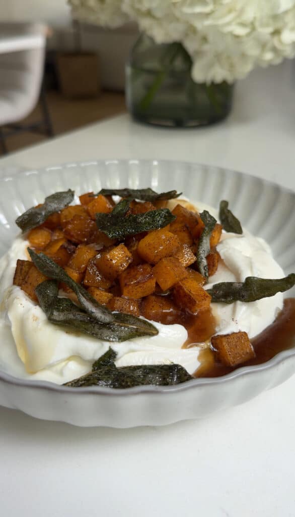 Roasted Butternut Squash dip in a white serving bowl on a white counter with flowers in the background.