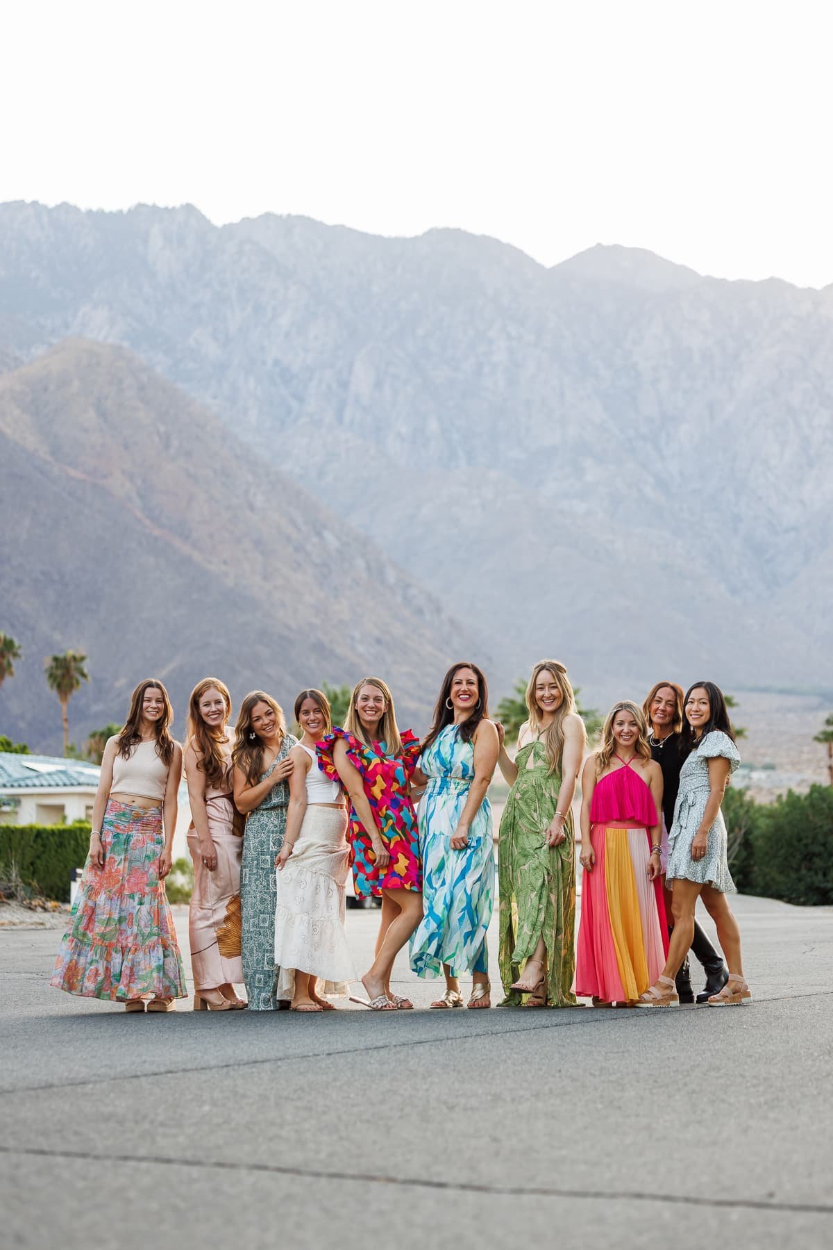 a group of women wearing dresses posing in front of the mountains.