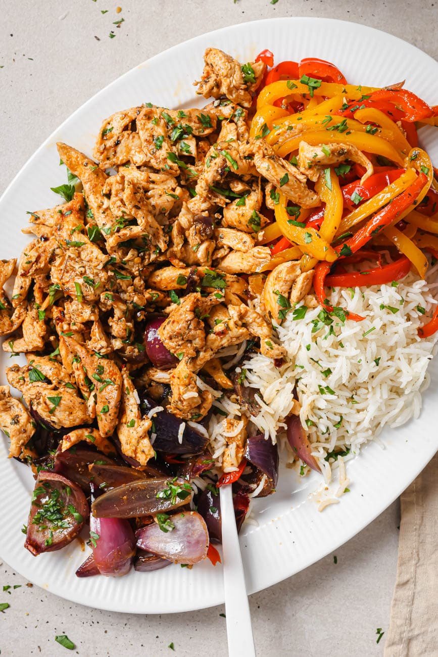 Top down view of a plate with baked chicken and peppers with white rice.