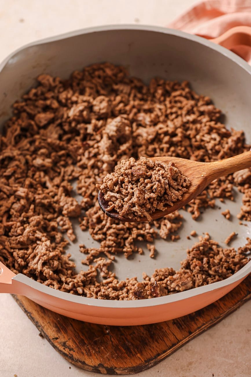 Browned ground beef in a skillet with a wooden spoon.