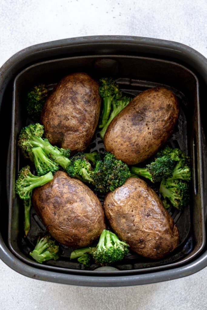 Russet potatoes and broccoli florets in an air fryer basket.