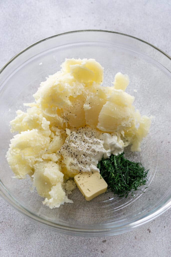 Potato insides, Greek yogurt, butter, dill, and seasonings in a clear mixing bowl.