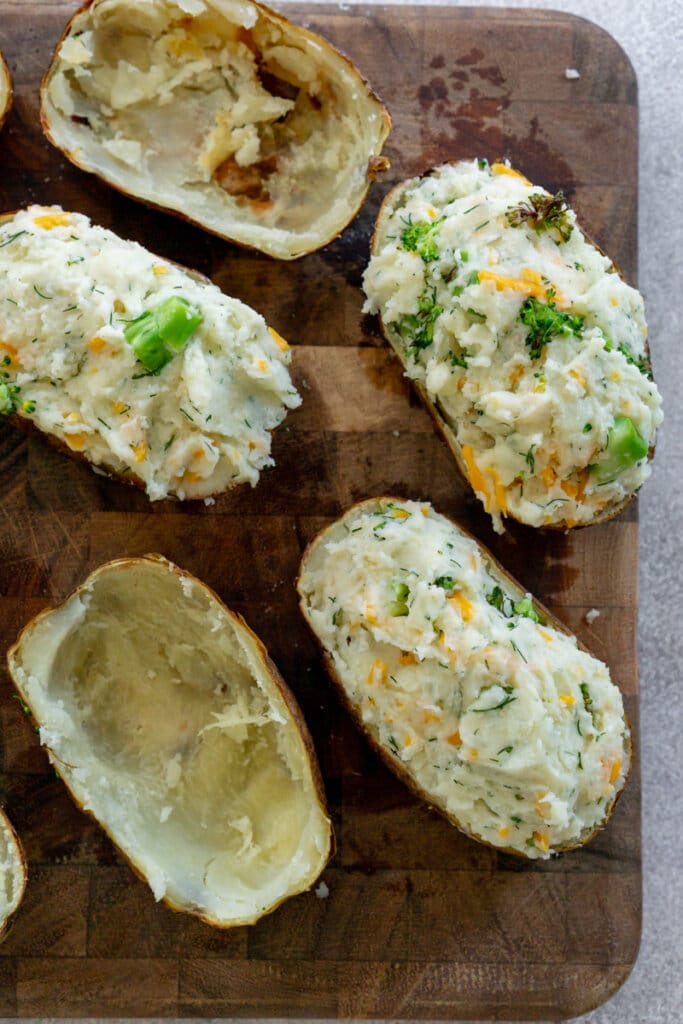 Twice baked potato mixture in hollow potato shells atop a cutting board.