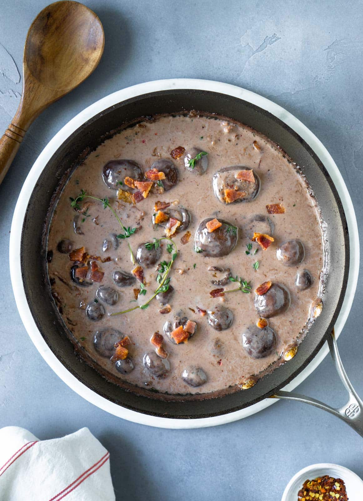 Gravy with bacon and mushroom in a pan next to a wooden spoon and dish towel.