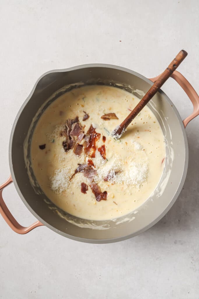 mixing bacon and cheese into a pot of corn chowder.