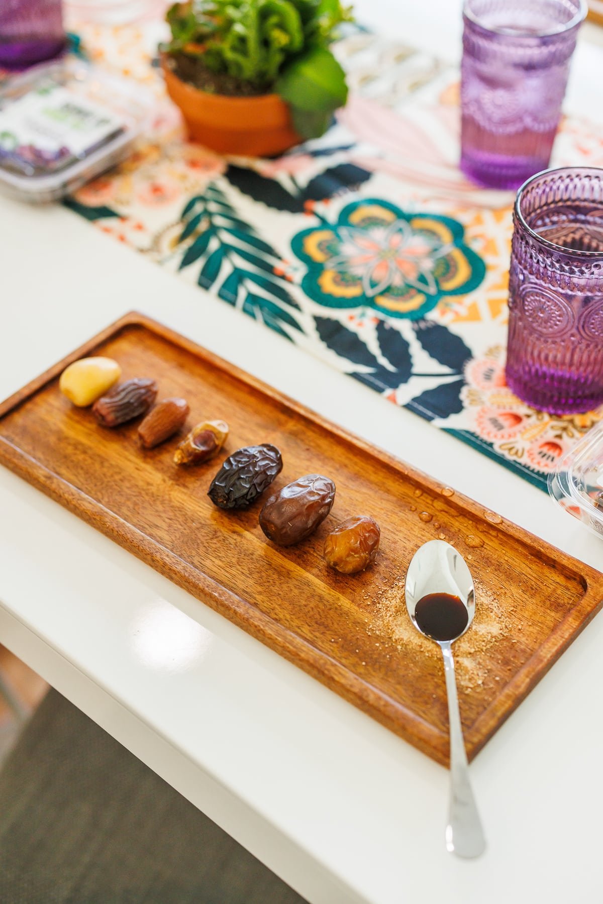 a flight of dates on a wood board with purple glasses nearby.