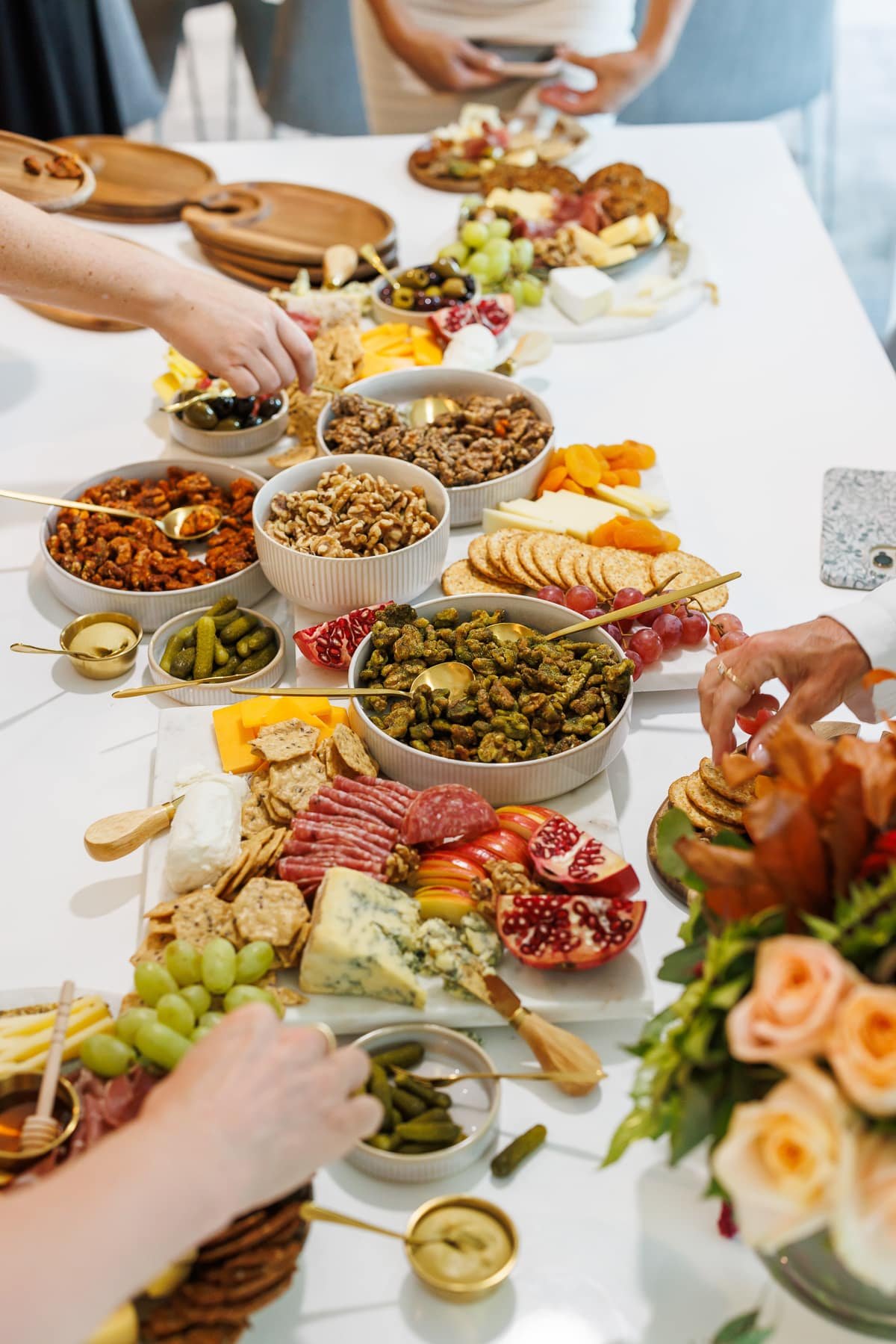 a grazing board laid out on a table with various fruits, nuts, and cheeses with hands grabbing at different items.