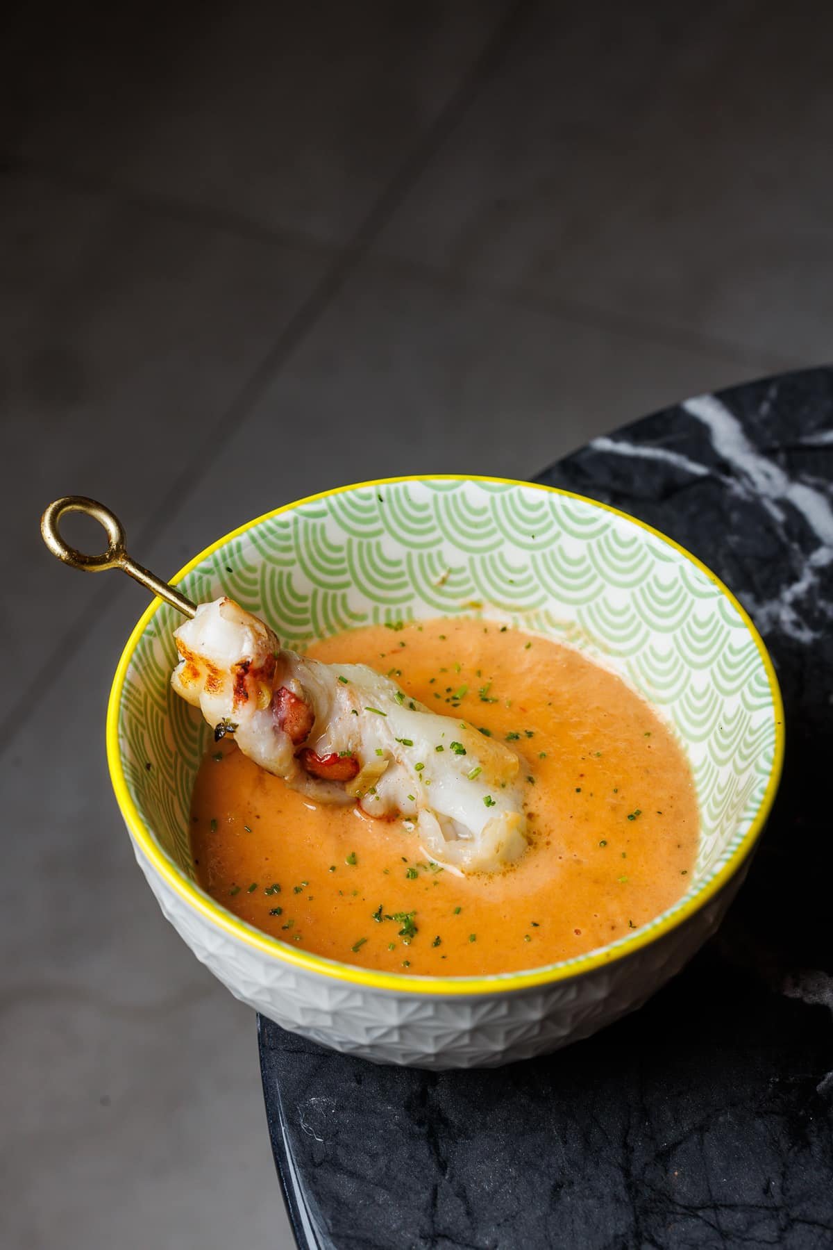 a bowl of lobster bisque with a grilled lobster tail on a skewer.