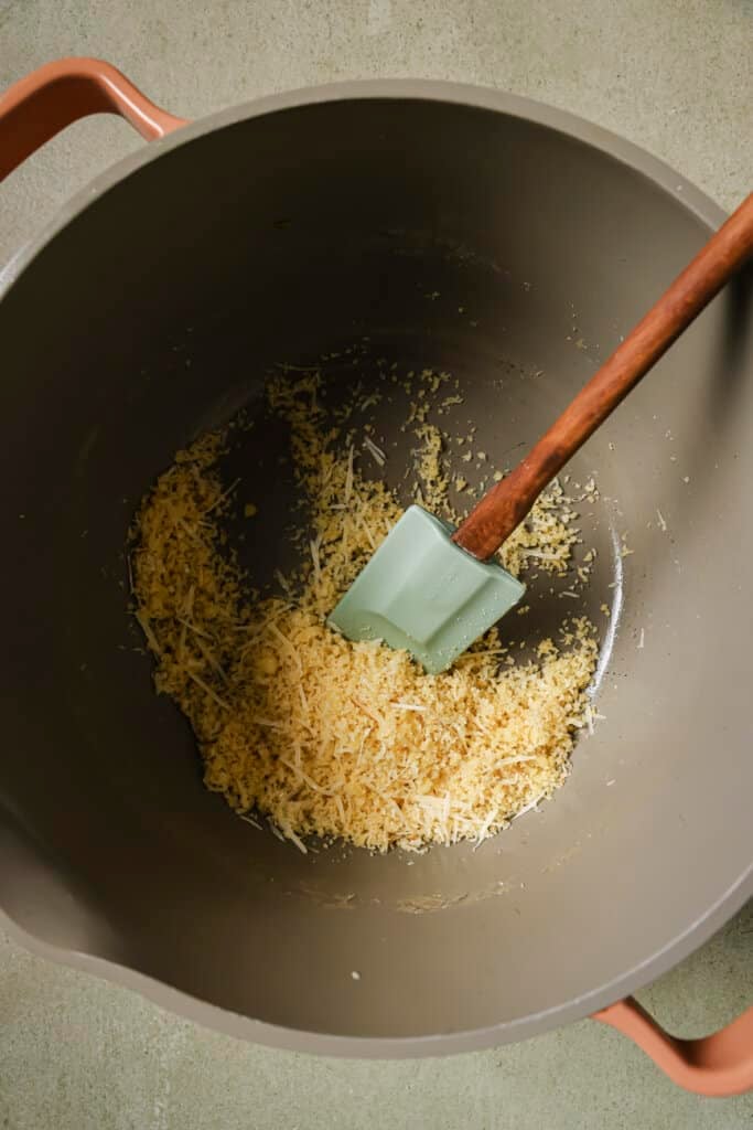 Stirring cheese with a rubber spatula in a skillet.