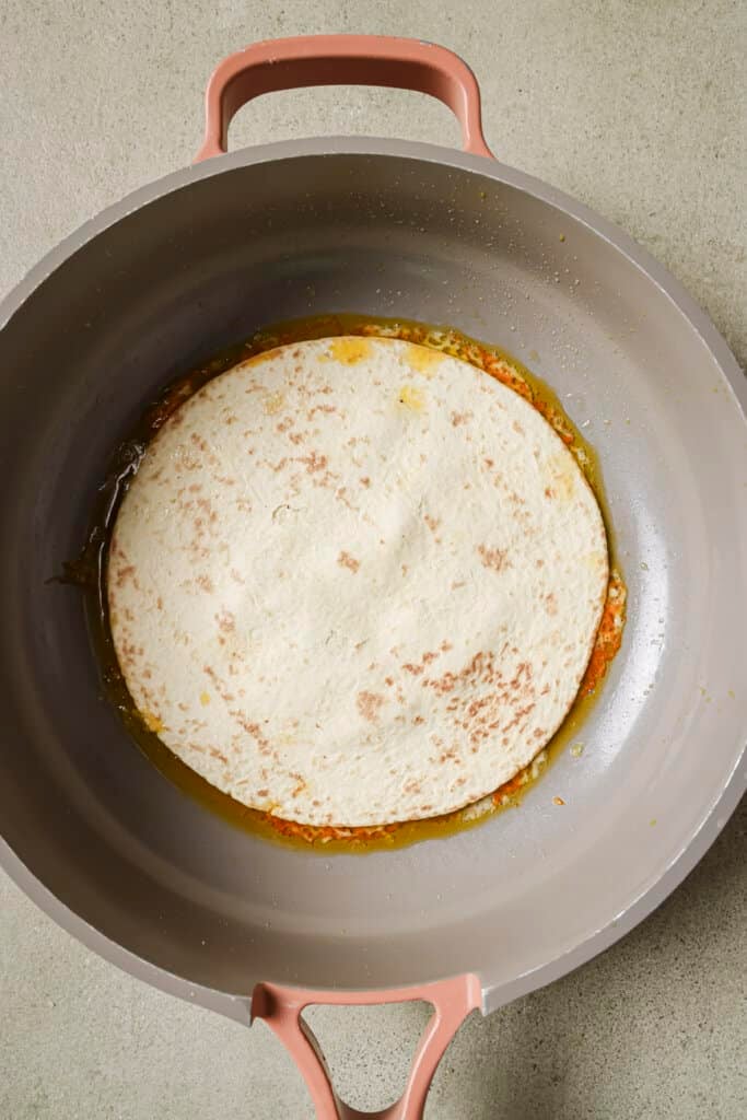 Adding a tortilla on top of cheese and turkey in a skillet.