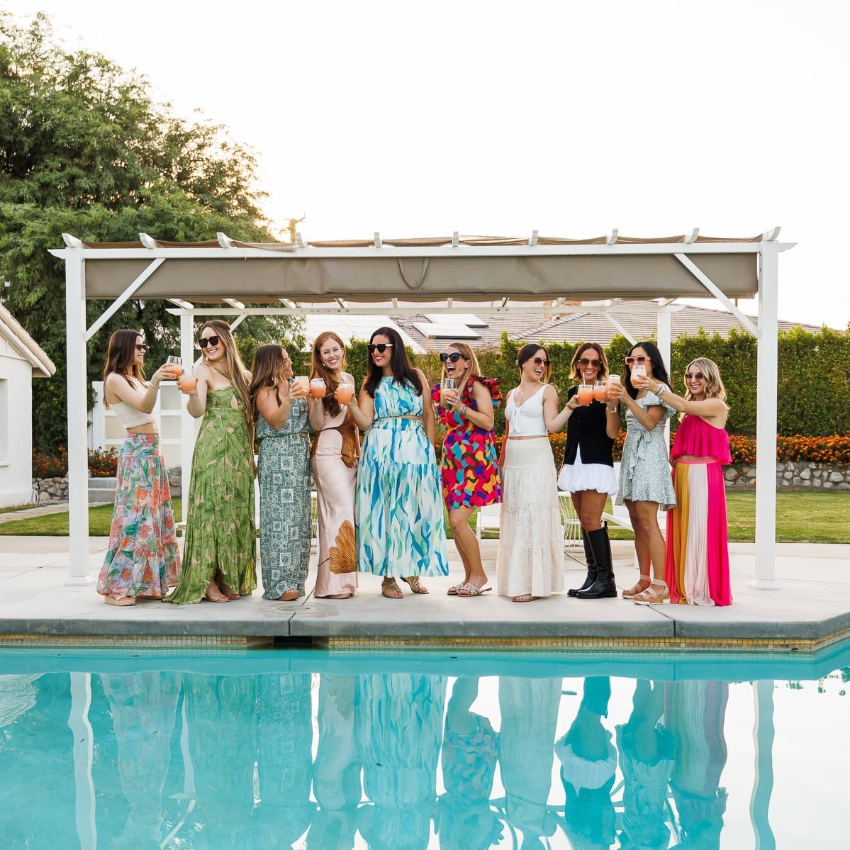 a group of women standing around a pool holding cocktails and laughing.