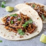 Turkey tacos garnished with cilantro and red onion with lime wedges.