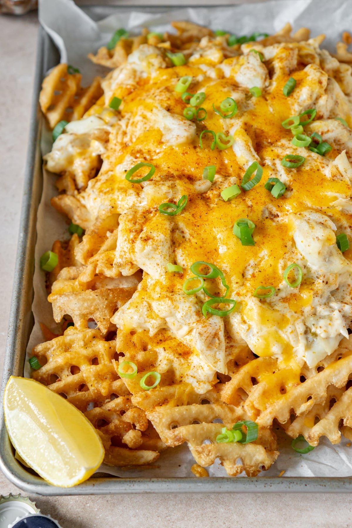 Close up of crab fries on a baking sheet with a lemon wedge for garnish.