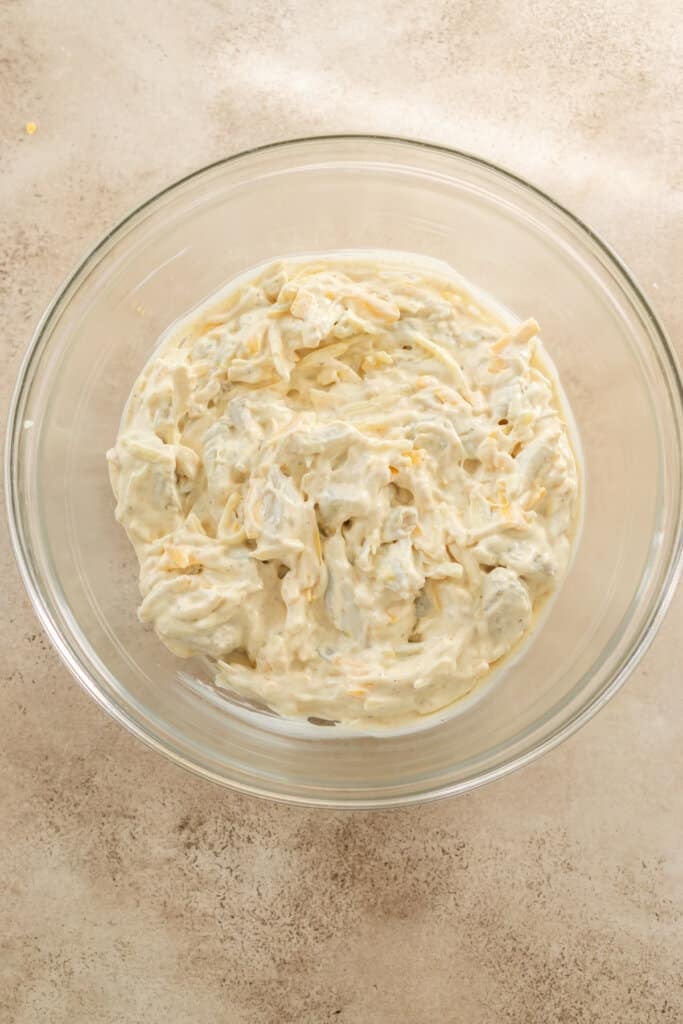 Mixing cream cheese and shredded cheese in a glass bowl.