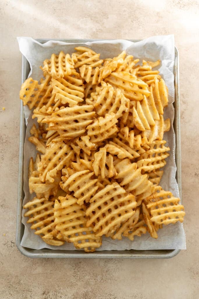 Golden brown waffle fries on a parchment lined baking sheet.