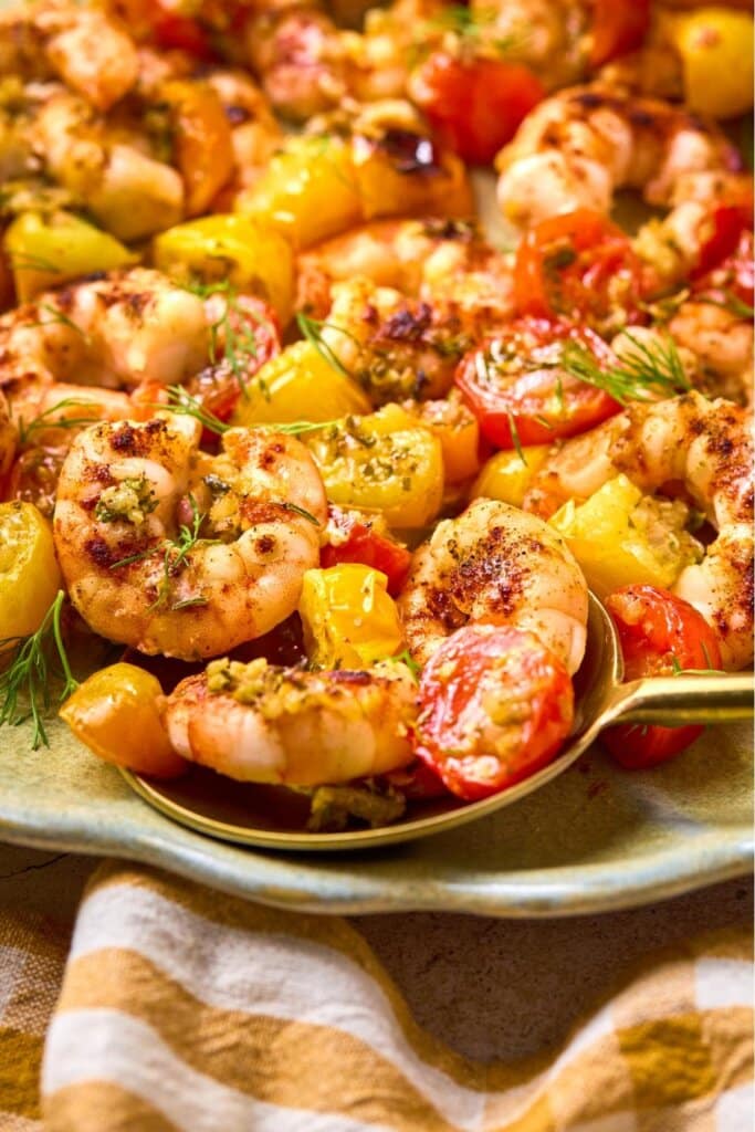 Close up shot of a golden spoon lifting up sheet pan shrimp from a dish.