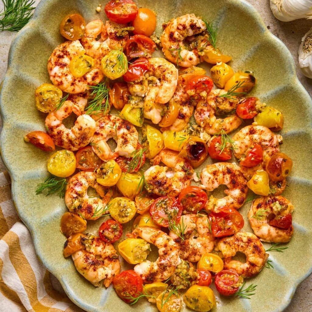 Square image featuring sheet pan shrimp in a shell-pattern green serving dish.