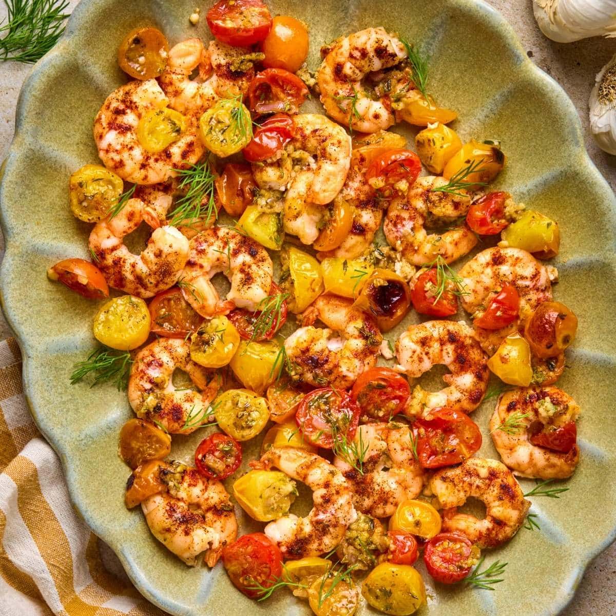 Square image featuring sheet pan shrimp in a shell-pattern green serving dish.