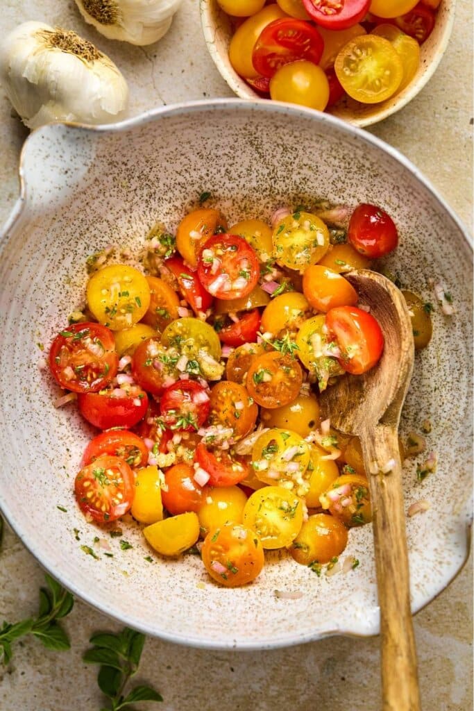 Mixing cherry tomatoes with seasonings in a bowl.