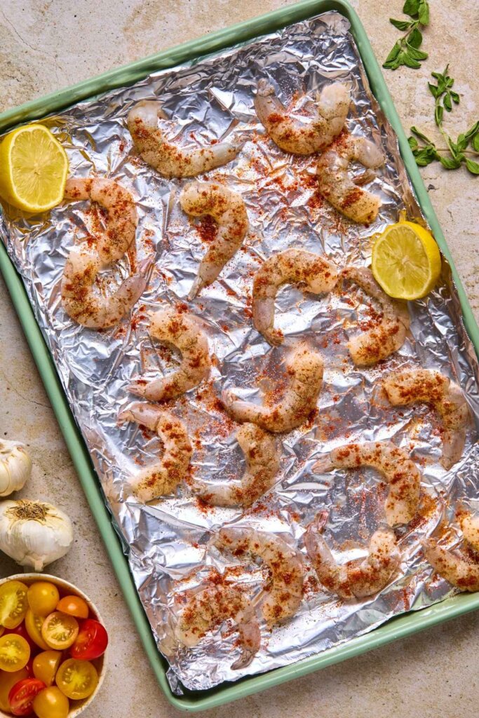 Seasoned raw shrimp on an aluminum covered baking sheet.