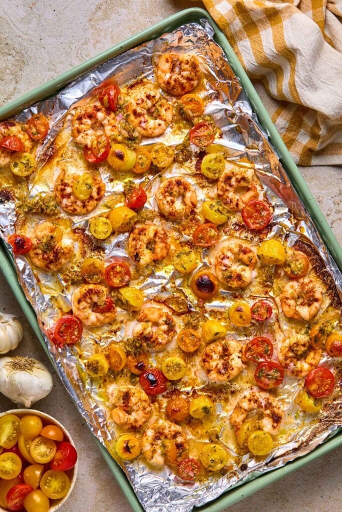 Fully cooked sheet pan shrimp with tomatoes on an aluminum covered baking sheet.